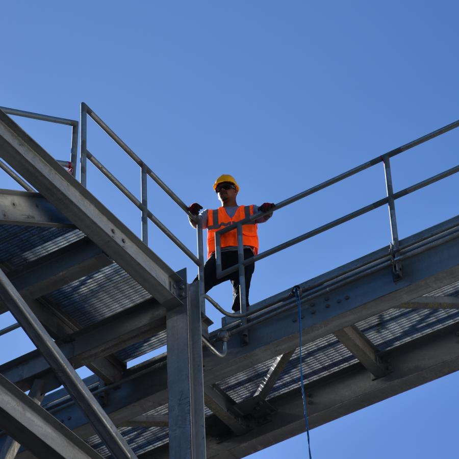 Construction worker standing on steel walkway against blue sky